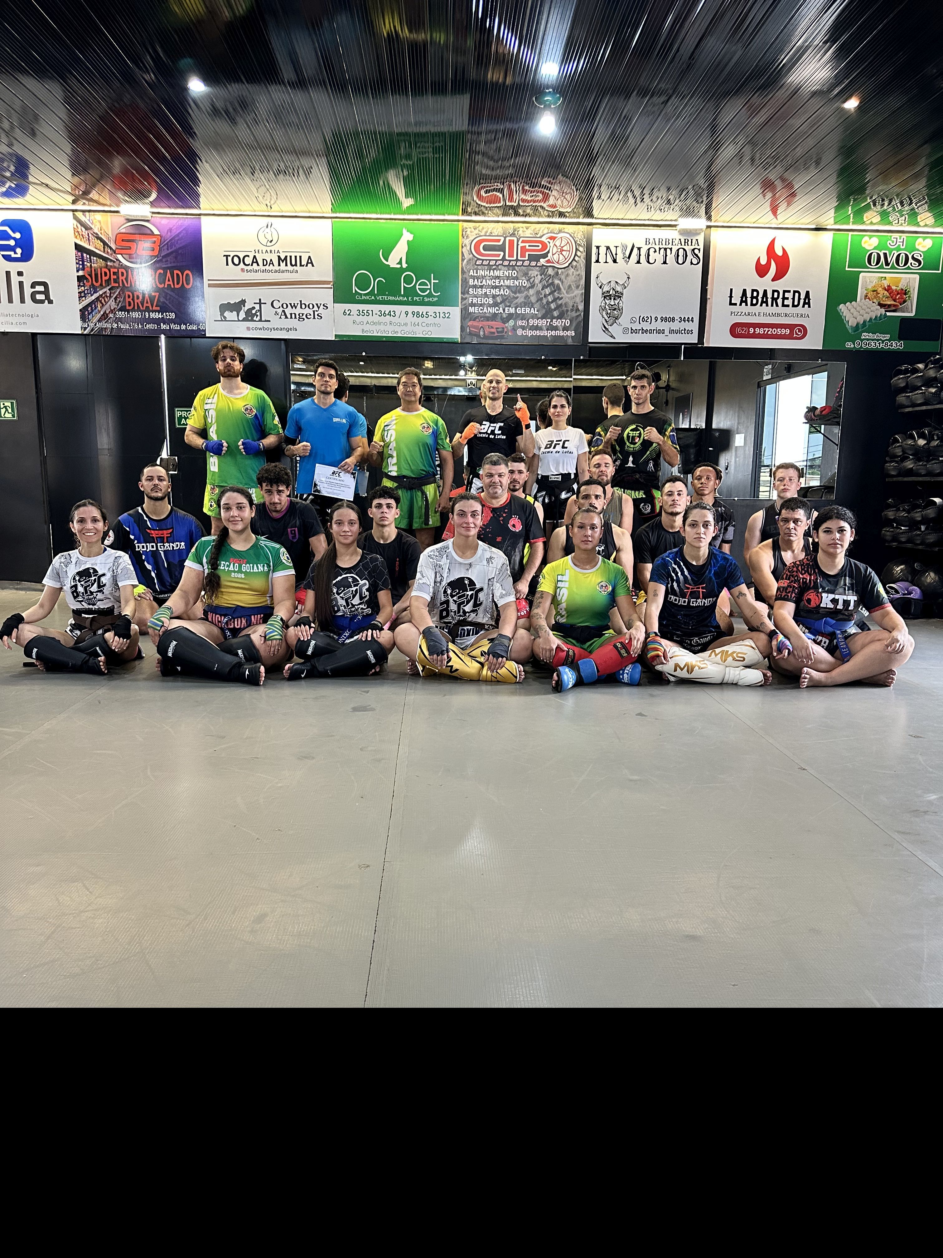 Foto em grupo com dezenas de alunos, atletas e instrutores de artes marciais sentados e em pé no tatame da BFC após o Seminário de K-1.