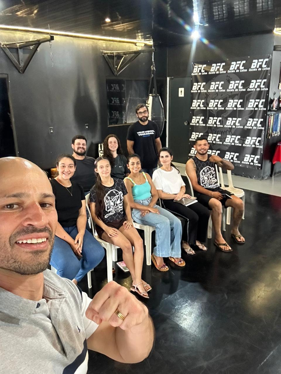 Instrutor Ernane Peixoto em primeiro plano sorrindo, ao lado de sua equipe de professores de artes marciais sentados na academia BFC.